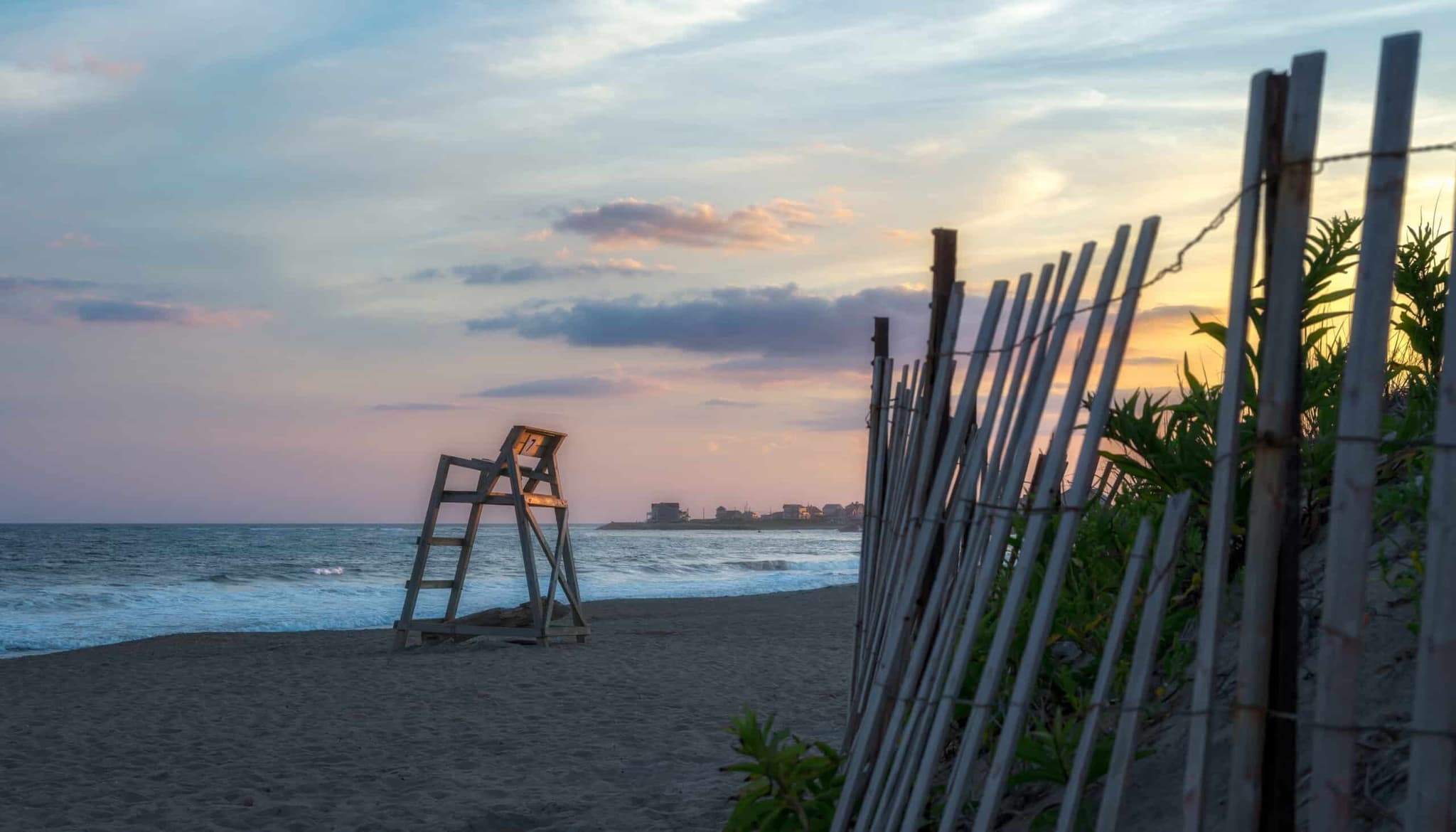 An empty beach with a lifeguard chair and dune fence
